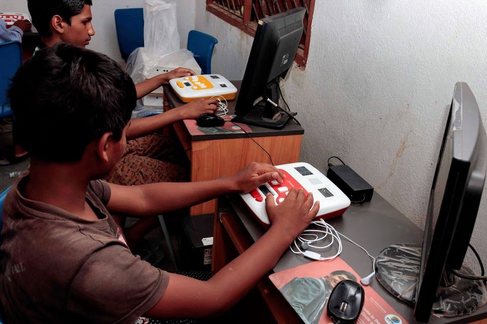 Two children are seated in front of computer monitors, using their respective Annies