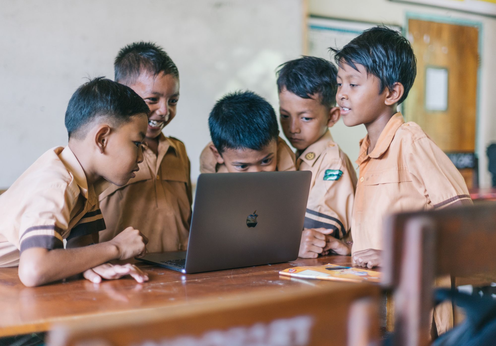 Five boys look intently at the screen of a laptop in their classroom