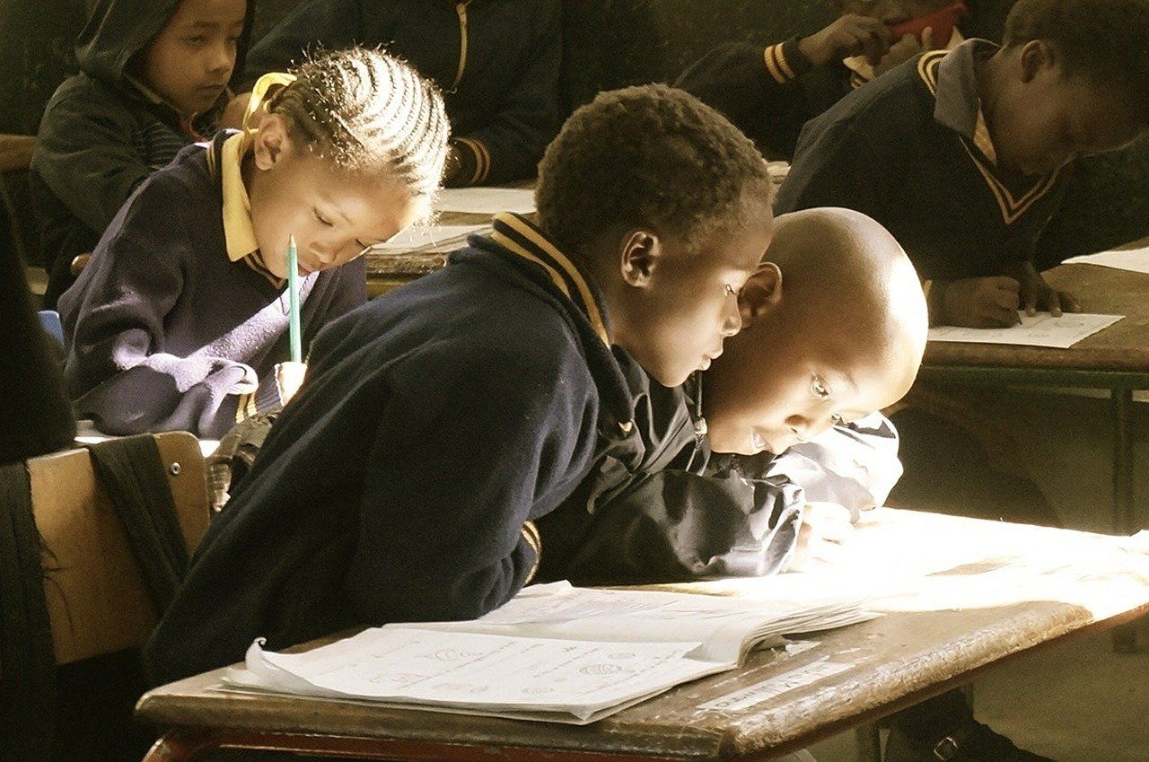 Several children in navy blue uniforms are intently working on their books at their benches