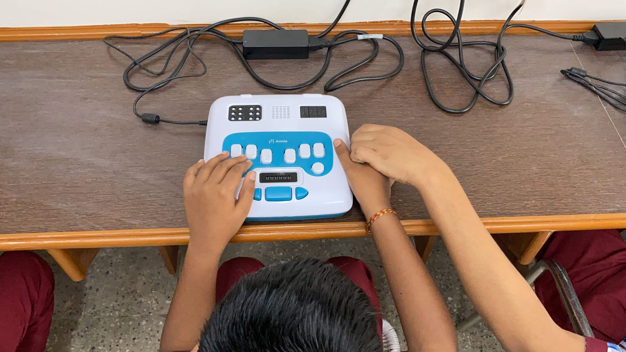 A child uses the Annie Braille learning device, assisted by their teacher