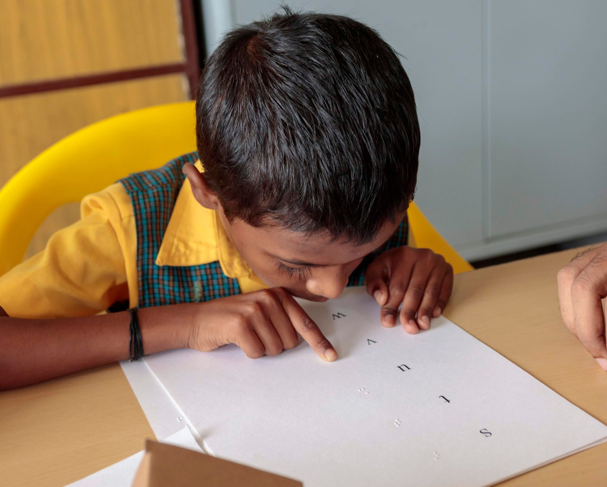 A child reads the English alphabet from a sheet of paper with Braille text