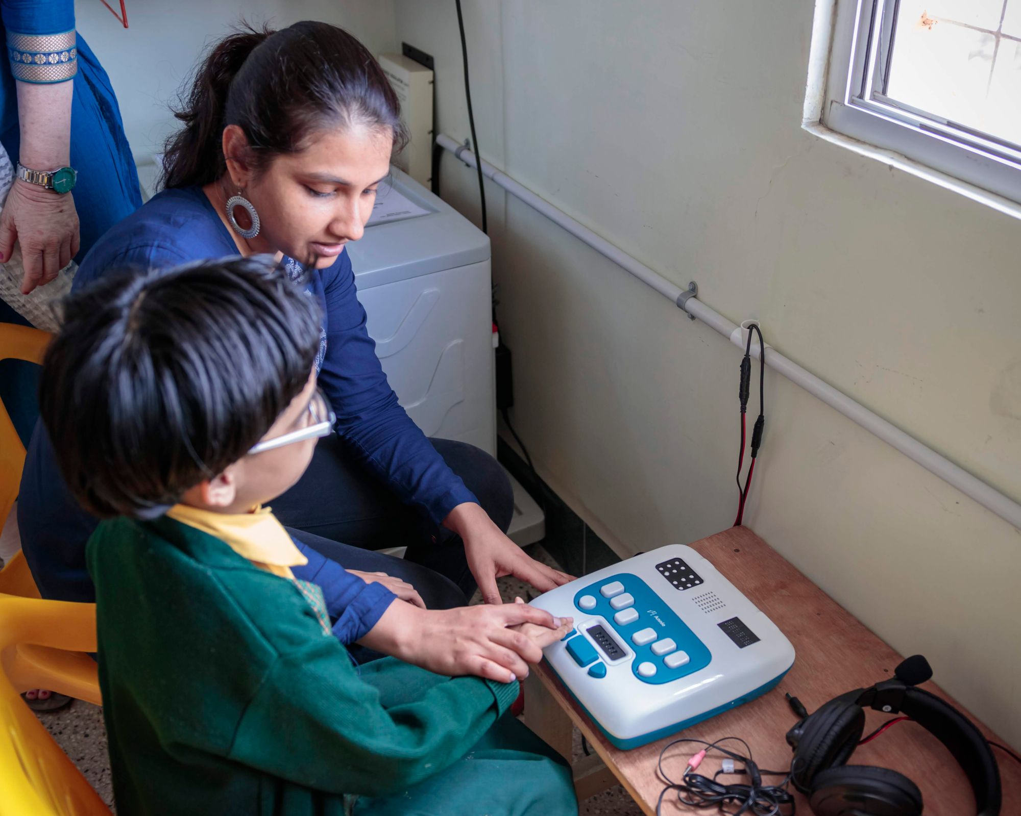 A member of the Thinkerbell Labs team guides a student in uniform to press the appropriate buttons on Annie