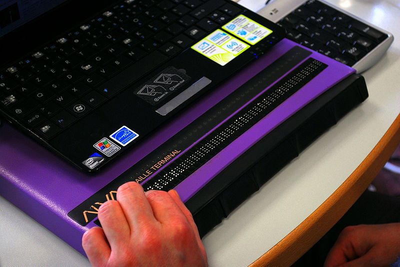 A person is reading on their refreshable Braille display along with a laptop