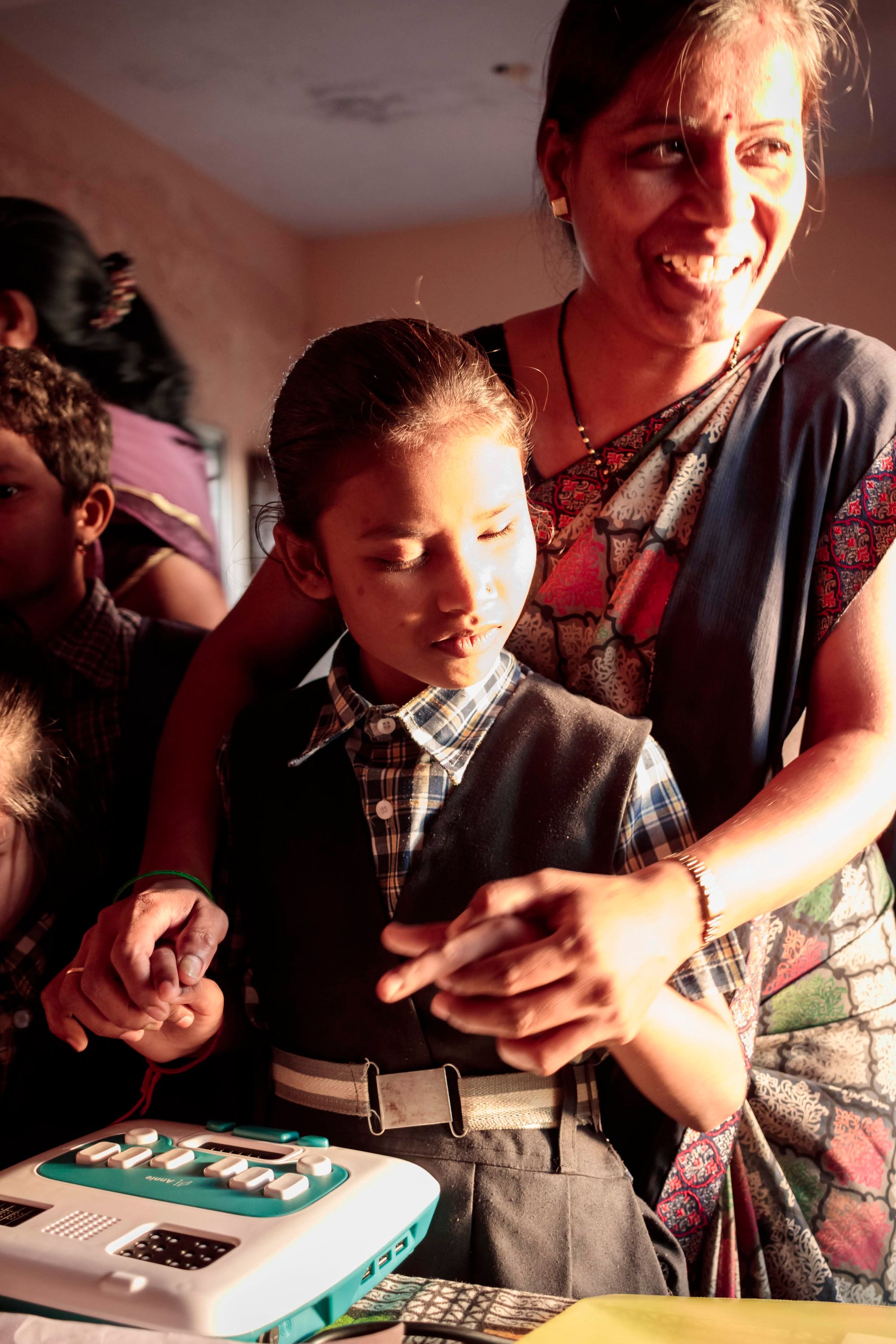 A teacher guides her student's fingers to use Annie to learn Braille. The teacher is smiling