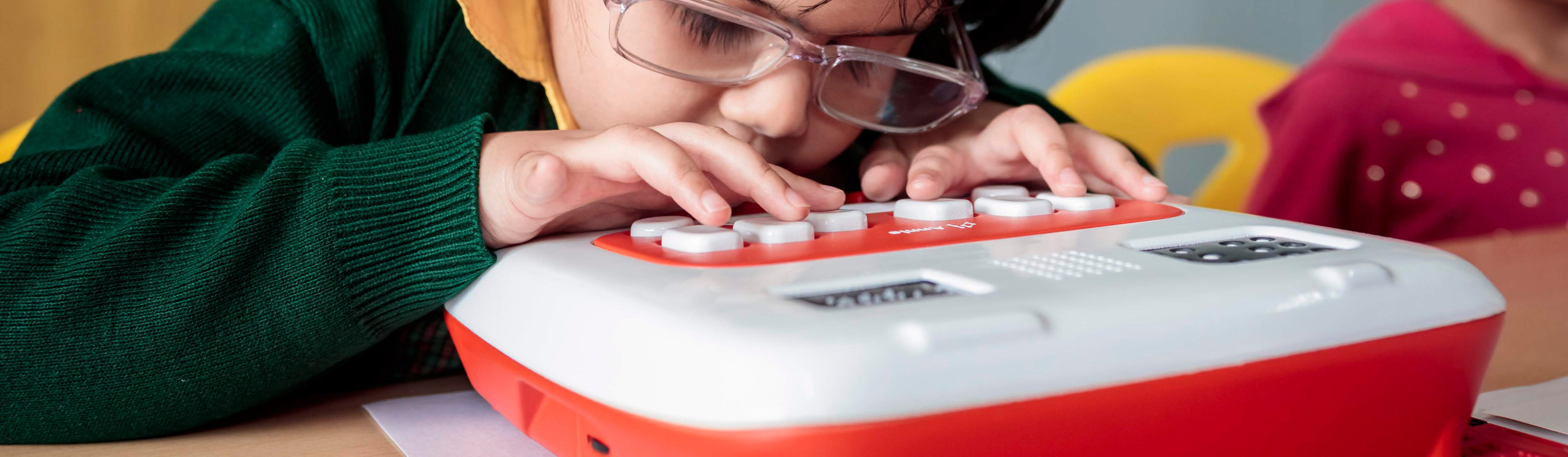 A young student with glasses leaning close to read braille on Annie’s keys
